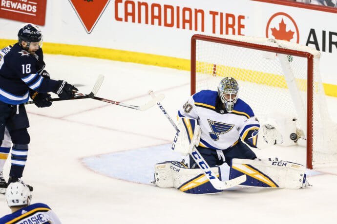 St. Louis Blues goalie makes a save with Winnipeg Jets forward at Bell MTS Place